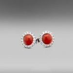 A pair of BUNDA 'Valentin' Precious Coral Earrings in Platinum. Each earring is set with a round cabochon of natural precious coral with castle-set round brilliant diamonds to the head.  Fittings are post and butterfly in platinum.   Characteristics of Red Cabochon cut Corals: 2 = 9.76ct.  Characteristics of Additional Round Brilliant Cut Diamonds: 32 = .83ct, F colour, VS Clarity  Total weight: 6.29 grams.