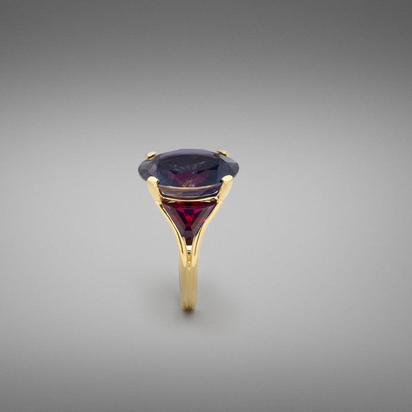 A BUNDA 'Bundova' Iolite and Rubellite Ring in 18ct yellow gold. The ring is set with a large round brilliant iolite in a four claw 18ct yellow gold setting. Two trapezoid cut rubellite tourmalines are bezel set to the shoulders. The shank is an 18ct yellow gold double wire wrap.  Characteristics of Iolite - 1 = 18.75cts  Characteristics of Rubellite Tourmaline - 2 = 3.10cts  Weight of Ring = 13.30 grams