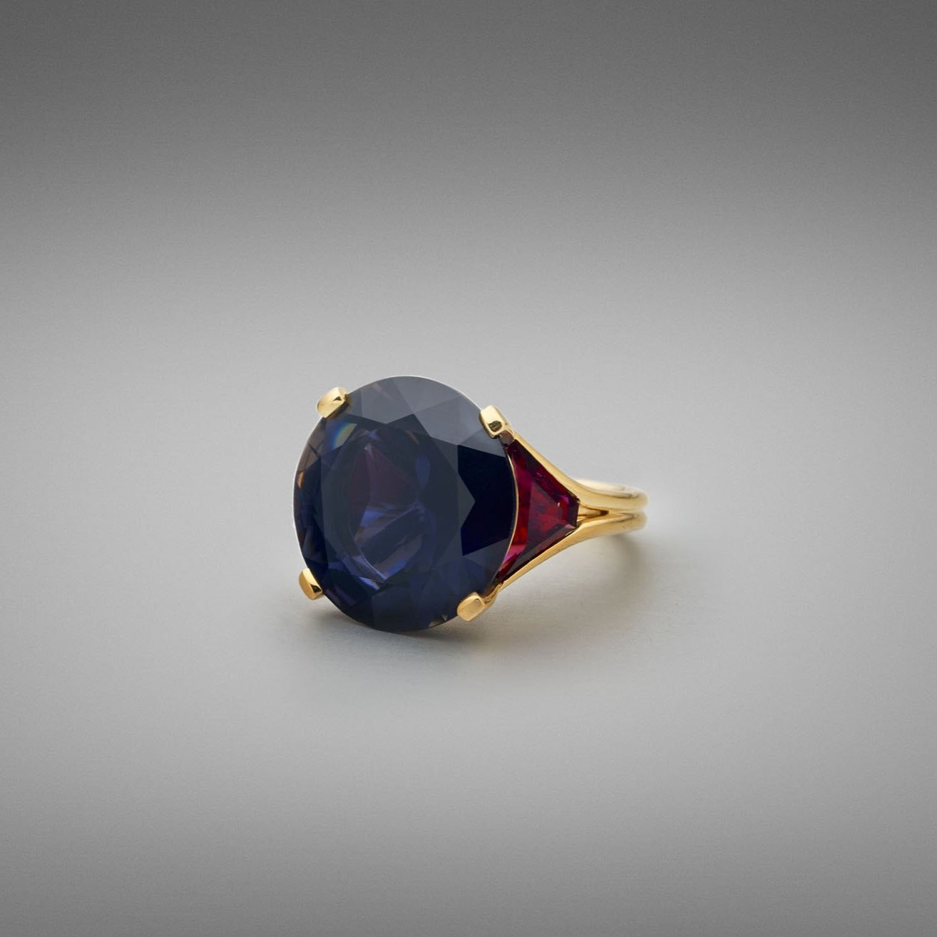 A BUNDA 'Bundova' Iolite and Rubellite Ring in 18ct yellow gold. The ring is set with a large round brilliant iolite in a four claw 18ct yellow gold setting. Two trapezoid cut rubellite tourmalines are bezel set to the shoulders. The shank is an 18ct yellow gold double wire wrap.  Characteristics of Iolite - 1 = 18.75cts  Characteristics of Rubellite Tourmaline - 2 = 3.10cts  Weight of Ring = 13.30 grams