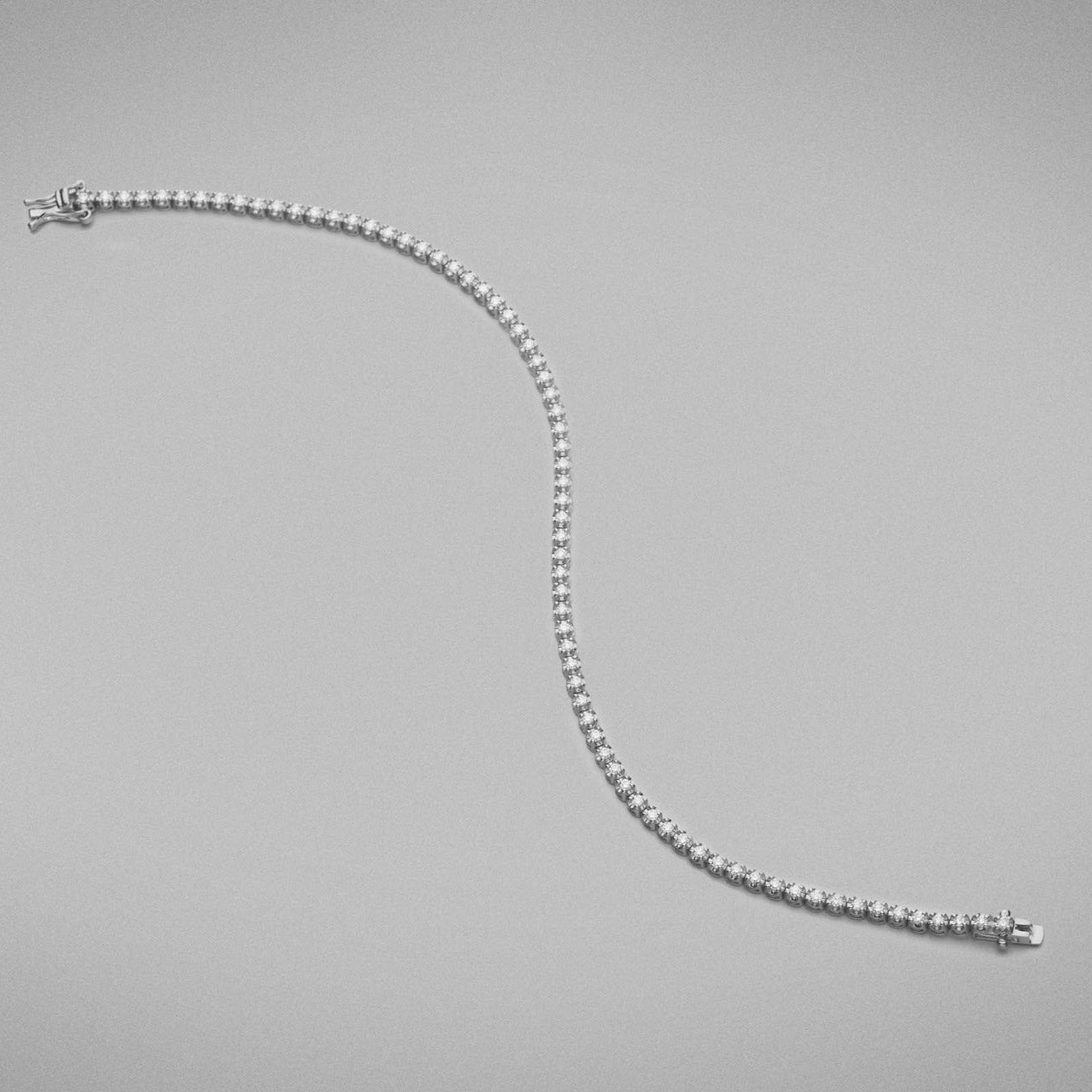 A BUNDA 'Tennis' bracelet in 18ct white gold. The bracelet is set with round brilliant diamonds in castle claw settings. Bracelet is stamped 'BUNDA'.  Characteristics of Round Brilliant Cut Diamonds: 87 = .69ct, F colour, VS Clarity  Total weight of bracelet: 5.19 grams