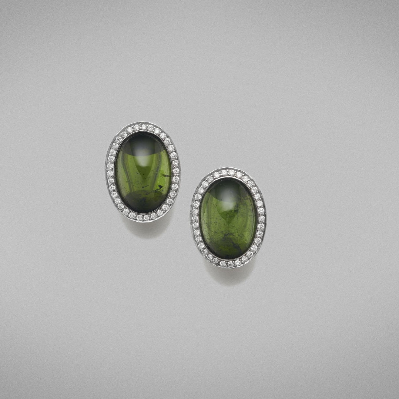 A pair of BUNDA 'Corvus' tourmaline earrings in 18ct white gold, featuring a pair of cabochon cut green tourmalines, bezel set and surrounded with threadset round brilliant cut diamonds, fitted with a post and keyhole clip fitting.  Weight of tourmalines: 2 = 14.50ct.  Characteristics of diamonds: 68 = 0.34ct, F colour, VS clarity.