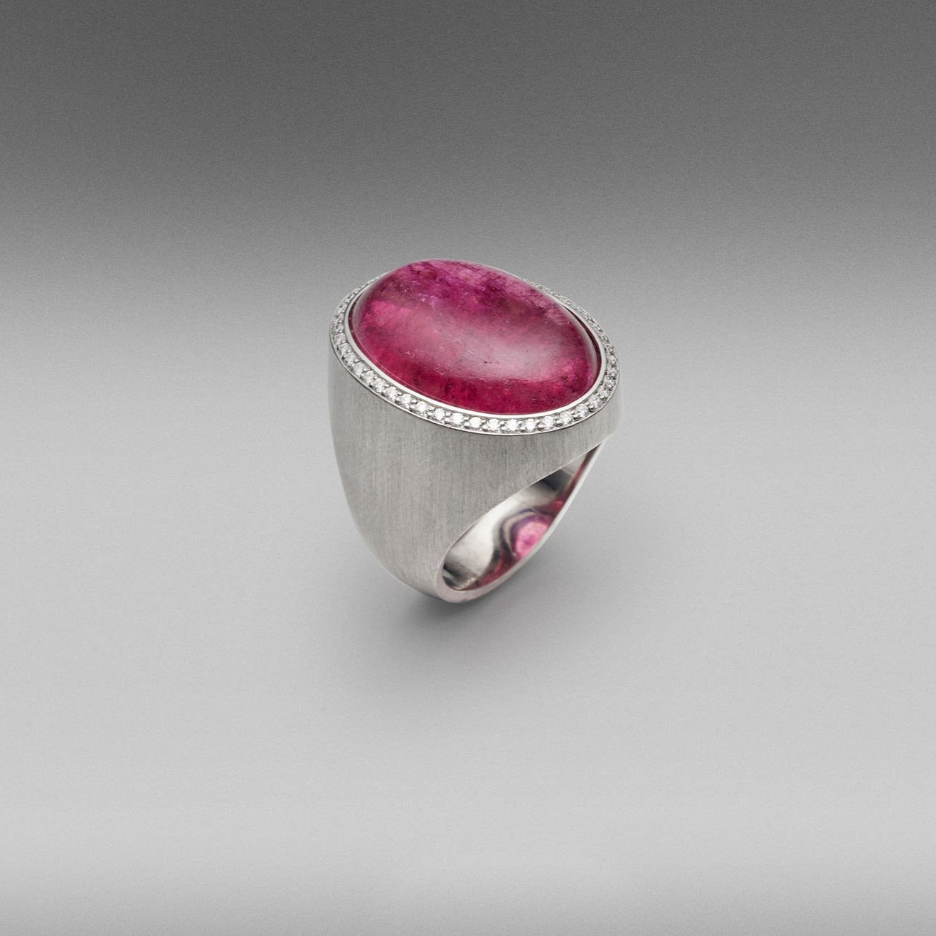 A BUNDA 'Corvus' ring in 18 carat white gold, set with a cabochon cut Tourmaline, surrounded with a line of thread set diamonds. The white gold setting has an elegant brushed finish.  Weight of Tourmaline: 1 =24.15ct.  Characteristics of diamonds: 45 = 0.25ct, F colour, VS clarity.  Total weight: 21.38g