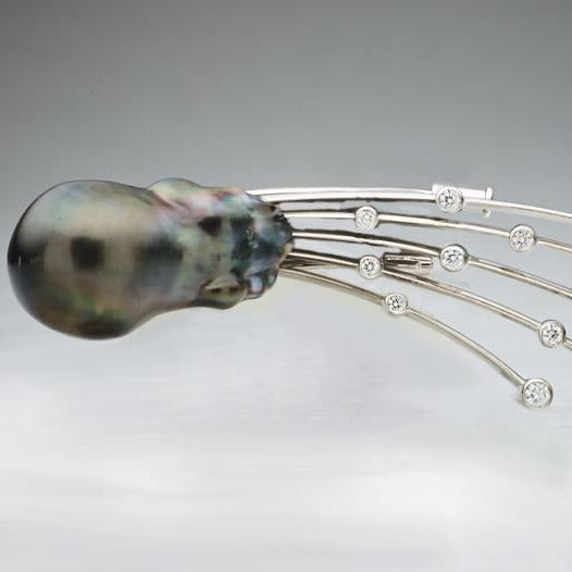 A BUNDA 'Meteor' pearl and diamond brooch, set with a large baroque shaped Cultured Tahitian pearl, trailing a tail of 18ct white gold bezel set round brilliant cut diamonds.  The pearl measures 16.40mm, is dark green in colour with tones of aubergine, a clean skin and an excellent lustre.  Characteristics of diamonds: 13 = 0.60ct. F colour, VS clarity.  Total weight of Brooch: 23.69 grams